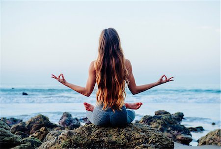 Rear view of young woman with long hair practicing lotus yoga pose on rocks at beach, Los Angeles, California, USA Stock Photo - Premium Royalty-Free, Code: 614-08641701