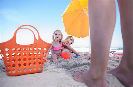 sharing umbrella - Two sisters sitting on beach, fathers legs, Cape Town, South Africa Stock Photo - Premium Royalty-Free, Code: 614-08641756