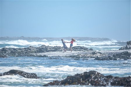 Distant view of young couple holding hands and spinning each other around on beach, Cape Town, South Africa Stock Photo - Premium Royalty-Free, Code: 614-08641763