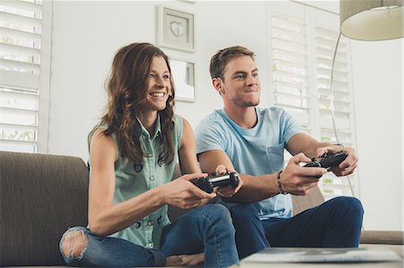 Couple on sofa using video game controller smiling Stock Photo - Premium Royalty-Free, Code: 614-08684858