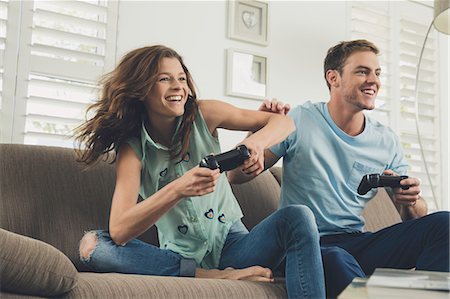 Couple on sofa using video game controller smiling Stock Photo - Premium Royalty-Free, Code: 614-08684859