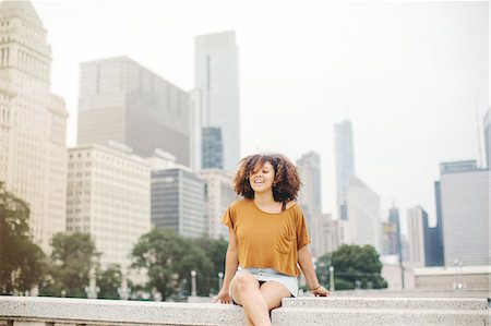 Woman sitting on wall in front of Chicago skyline smiling, Illinois Foto de stock - Sin royalties Premium, Código: 614-08685132