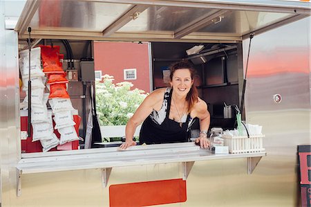 food stall - Portrait of woman leaning forward at hatch of food stall trailer Stock Photo - Premium Royalty-Free, Code: 614-08726394