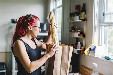 Young woman with pink hair unpacking baguette from shopping bag in kitchen Foto de stock - Sin royalties Premium, Código: 614-08726732