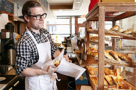 Male worker in bakery, putting baked goods into paper bag for customer Stock Photo - Premium Royalty-Free, Code: 614-08720526