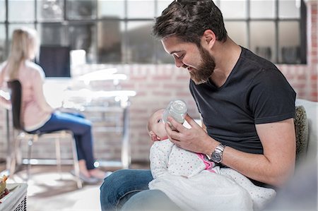 Father sitting, feeding baby daughter, mother sitting at desk, working, behind Stock Photo - Premium Royalty-Free, Code: 614-08720605