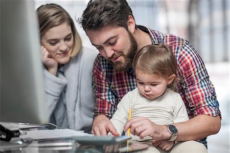 Couple sitting at desk, toddler sitting on man's lap watching man draw Stock Photo - Premium Royalty-Free, Code: 614-08720601