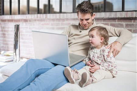 Father sitting on sofa with young daughter, looking at laptop Stock Photo - Premium Royalty-Free, Code: 614-08720610