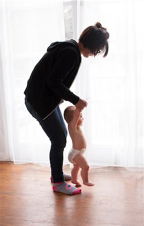 Young female babysitter helping baby boy toddle at home Stock Photo - Premium Royalty-Free, Code: 614-08826799