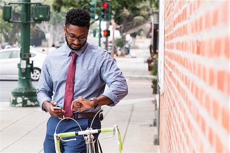 simsearch:614-08827048,k - Young man standing beside bicycle, using smartphone, looking at wristwatch Foto de stock - Sin royalties Premium, Código: 614-08827048