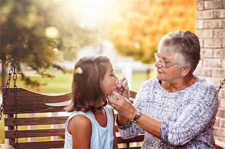 Grandmother and granddaughter sitting on porch swing, grandmother showing granddaughter how to apply lipstick Stock Photo - Premium Royalty-Free, Code: 614-08827109