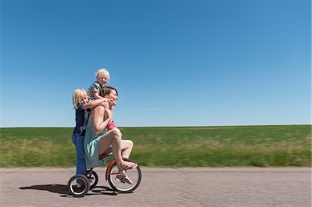 excess - Side view of mother and children riding tricycle in rural area Stock Photo - Premium Royalty-Free, Code: 614-08827151