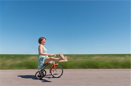 Side view of woman riding tricycle in rural area Fotografie stock - Premium Royalty-Free, Codice: 614-08827152