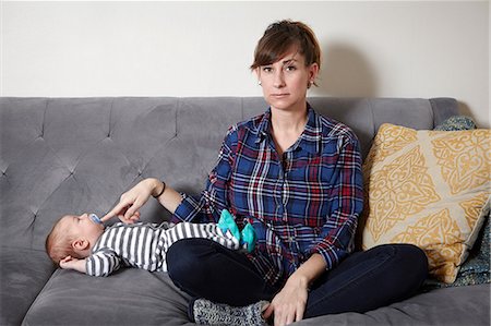 exhausted mother with baby - Mother sitting on sofa holding baby boy's pacifier in Stock Photo - Premium Royalty-Free, Code: 614-08827188