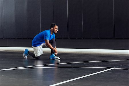 simsearch:614-08827236,k - Male basketball player tying trainer laces on basketball court Foto de stock - Royalty Free Premium, Número: 614-08827249