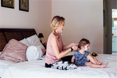 Woman sitting on bed plaiting toddler daughter's hair Stock Photo - Premium Royalty-Free, Code: 614-08821165