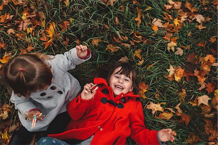 Overhead portrait of girl and toddler sister lying on grass and autumn leaves Stock Photo - Premium Royalty-Free, Code: 614-08821439