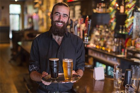 Portrait of young male bartender carrying tray of beer in public house Stock Photo - Premium Royalty-Free, Code: 614-08821482
