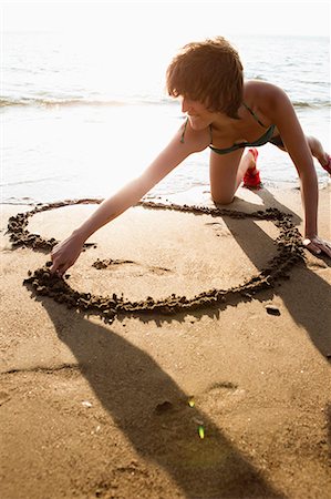 Woman drawing heart in sand on beach Stock Photo - Premium Royalty-Free, Code: 614-08868196