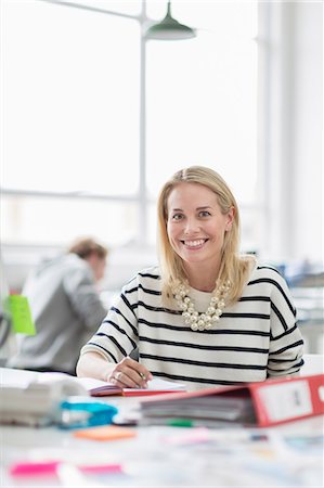 simsearch:614-08875120,k - Young woman sitting at desk and smiling in creative office, portrait Photographie de stock - Premium Libres de Droits, Code: 614-08874885