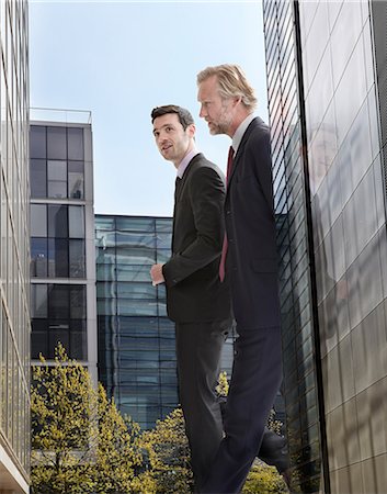 Oversized businessmen walking amongst skyscrapers, low angle view Stock Photo - Premium Royalty-Free, Code: 614-08875292