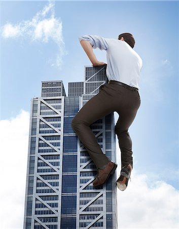 Oversized businessman climbing skyscraper, low angle view Stock Photo - Premium Royalty-Free, Code: 614-08875293