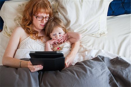 Mother and daughter lying in bed, looking at digital tablet Stock Photo - Premium Royalty-Free, Code: 614-08875425