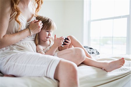 simsearch:614-08875430,k - Woman and girl sitting on bed looking at smartphone Fotografie stock - Premium Royalty-Free, Codice: 614-08875430