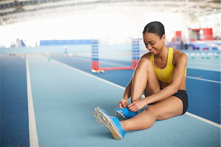 Young female athlete sitting on floor tying shoelace Stock Photo - Premium Royalty-Free, Code: 614-08875896