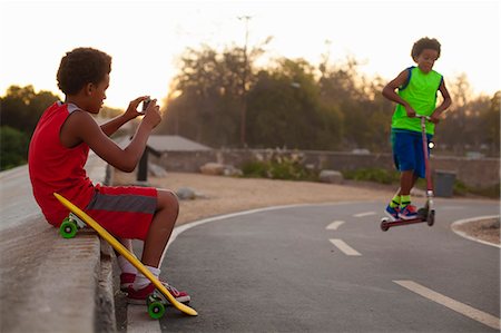 Boy photographing brother doing push scooter jump on road Stock Photo - Premium Royalty-Free, Code: 614-08876769