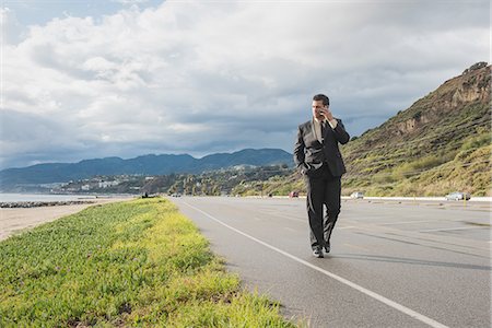 simsearch:614-08877313,k - Businessman strolling on coastal highway talking on smartphone Stock Photo - Premium Royalty-Free, Code: 614-08877314