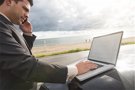 simsearch:614-08877313,k - Businessman talking on smartphone whilst using laptop at coastal parking lot Stock Photo - Premium Royalty-Free, Code: 614-08877317