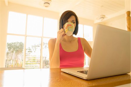 simsearch:614-08879232,k - Businesswoman drinking tablet whilst reading laptop in living room Photographie de stock - Premium Libres de Droits, Code: 614-08877404