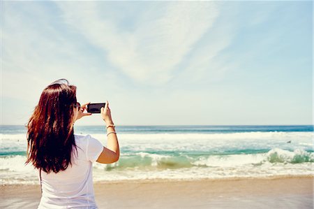 simsearch:614-08878321,k - Rear view of woman on beach taking photograph of the ocean Fotografie stock - Premium Royalty-Free, Codice: 614-08877651