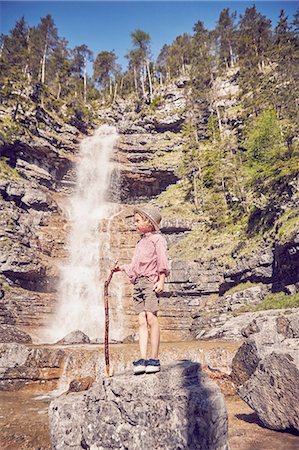 simsearch:614-08877972,k - Young boy, standing on rock beside waterfall, holding stick Fotografie stock - Premium Royalty-Free, Codice: 614-08877979