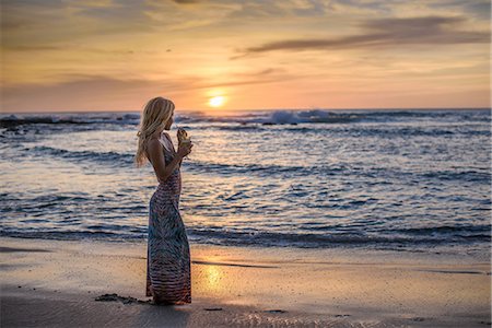 Young woman drinking cocktail on beach at sunset, Tamarindo, Costa Rica Stock Photo - Premium Royalty-Free, Code: 614-08878052