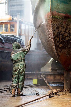 Rear view of worker cleaning boat with high pressure hose in shipyard Stock Photo - Premium Royalty-Free, Code: 614-08878559