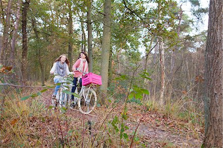 simsearch:614-08684819,k - Teenage girls in forest cycling on bicycles with pink crate attached Foto de stock - Royalty Free Premium, Número: 614-08879041