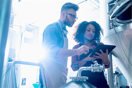 Low angle view of colleagues in brewery by conical fermentation tank side by side looking at digital tablet Stock Photo - Premium Royalty-Free, Code: 614-08879222