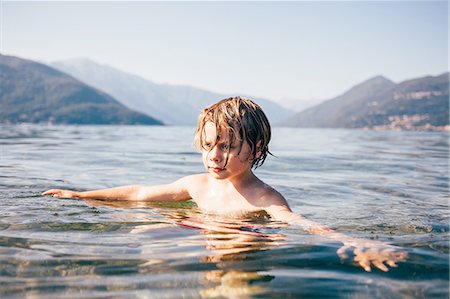 Mountain range and head and shoulders of boy in water arms open looking away, Luino, Lombardy, Italy Stock Photo - Premium Royalty-Free, Code: 614-08879257