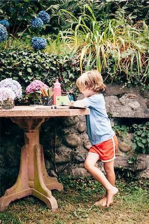 Side view of boy leaning against table in garden colouring, Luino, Lombardy, Italy Stock Photo - Premium Royalty-Free, Code: 614-08879265