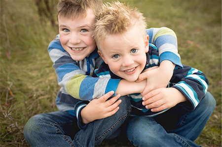 simsearch:632-05760167,k - Cropped view of boys sitting on grass hugging, looking at camera smiling Stock Photo - Premium Royalty-Free, Code: 614-08879313