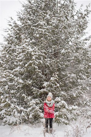 Young girl standing in front of large evergreen tree, covered in snow Stock Photo - Premium Royalty-Free, Code: 614-08879388