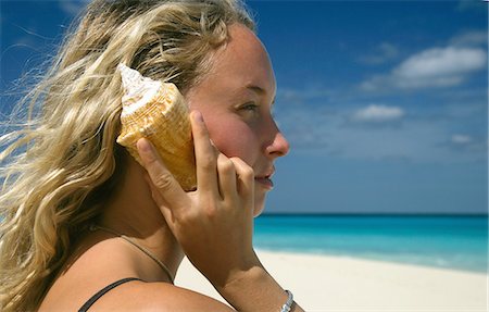 paradise island bahamas beach - Woman holding shell by ear at beach Stock Photo - Premium Royalty-Free, Code: 614-08870307
