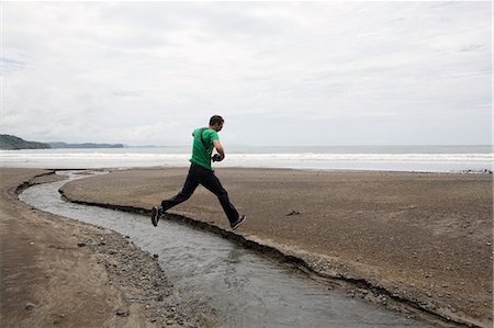 Man jumping over stream on beach Stock Photo - Premium Royalty-Free, Code: 614-08872054