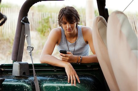 Teenager leaning against jeep checking phone Stock Photo - Premium Royalty-Free, Code: 614-08873158