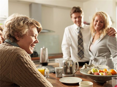 Teenage son sitting at kitchen table with parents in background Photographie de stock - Premium Libres de Droits, Code: 614-08873615