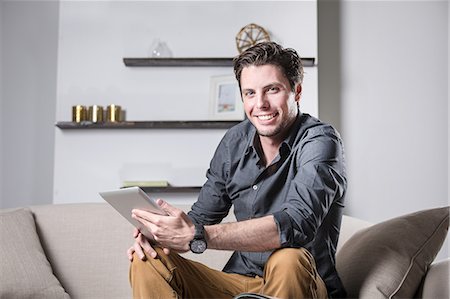 empresario (hombre) - Portrait of young man sitting on sofa, holding digital tablet, smiling Foto de stock - Sin royalties Premium, Código: 614-08884719