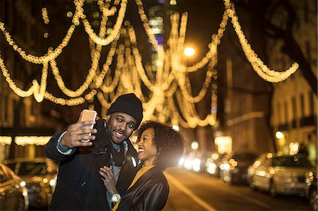 Couple taking smartphone selfie by Christmas lights at night, New York, USA Stock Photo - Premium Royalty-Free, Code: 614-08884753