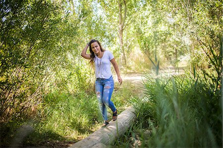 Portrait of teenage girl stepping across log in woodland Stock Photo - Premium Royalty-Free, Code: 614-08884992